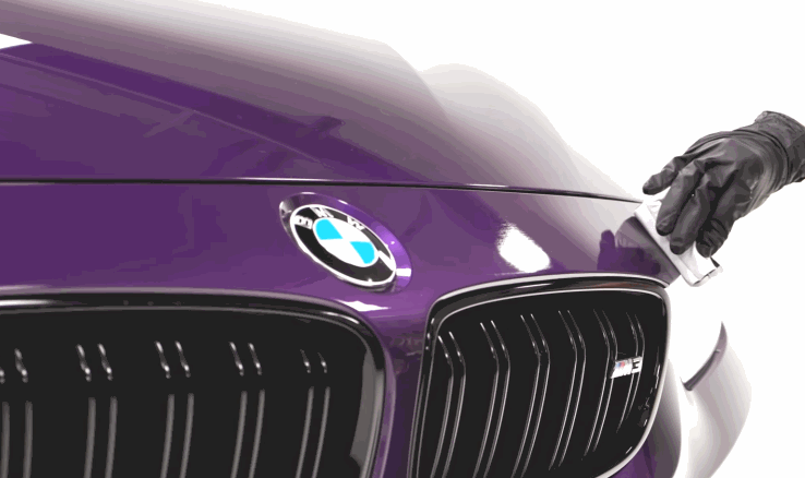 A gloved hand applies ceramic coating to the hood of a purple BMW, creating a high-gloss finish and protective layer.