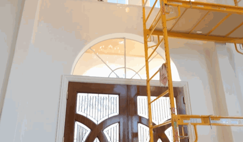Interior view of a tall home entryway with a yellow scaffold positioned in front of large arched windows, mid-installation of residential window tint.