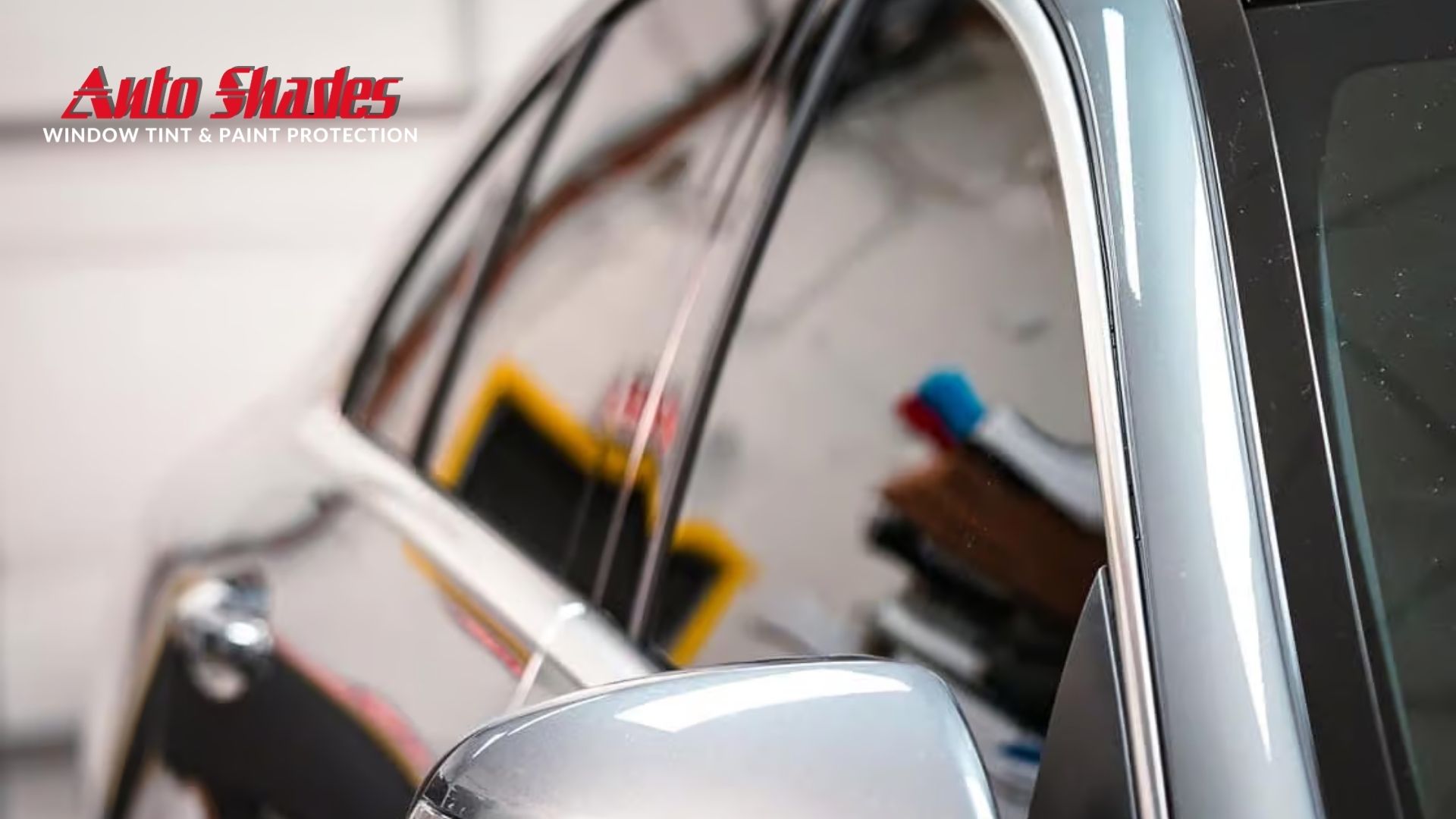 Close up of a car door with sleek ceramic window tint applied, reflecting a clean workshop environment.